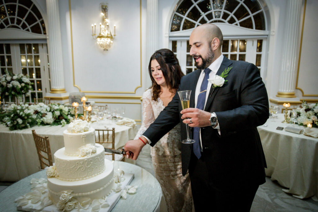 Newlywed couple cutting wedding cake together in Crystal Plaza gold ballroom reception