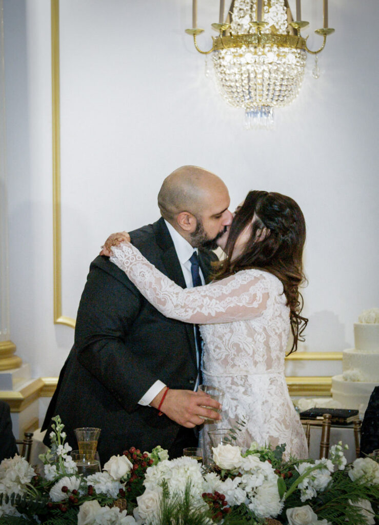 Newlywed couple sharing a kiss at sweetheart table with white floral centerpiece at Crystal Plaza NJ