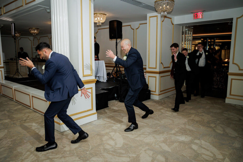 Groomsmen in navy suits dancing and laughing at Crystal Plaza multicultural wedding reception