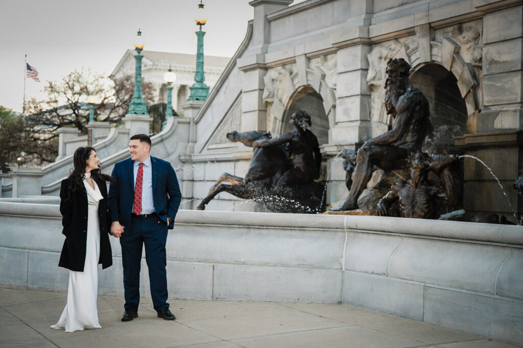 Engaged couple holding hands near the Neptune fountain at Library of Congress Washington DC