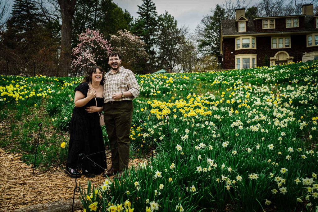 Newly engaged couple laughing together in front of spring daffodil field at Reeves-Reed Arboretum