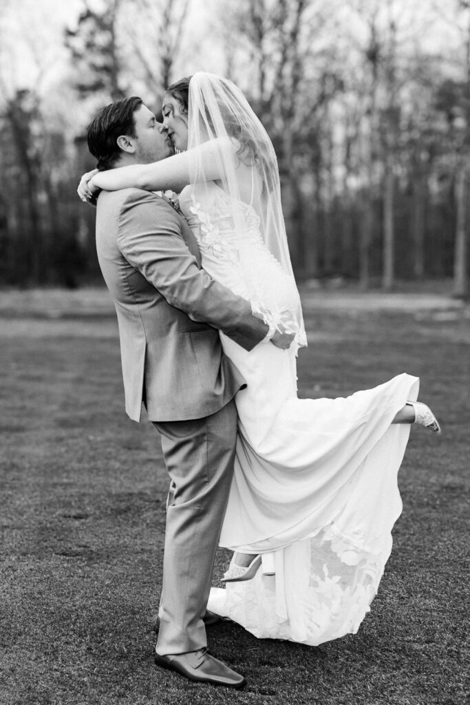 Black and white photo of groom lifting bride mid-kiss at outdoor Pinelands Golf Club wedding New Jersey