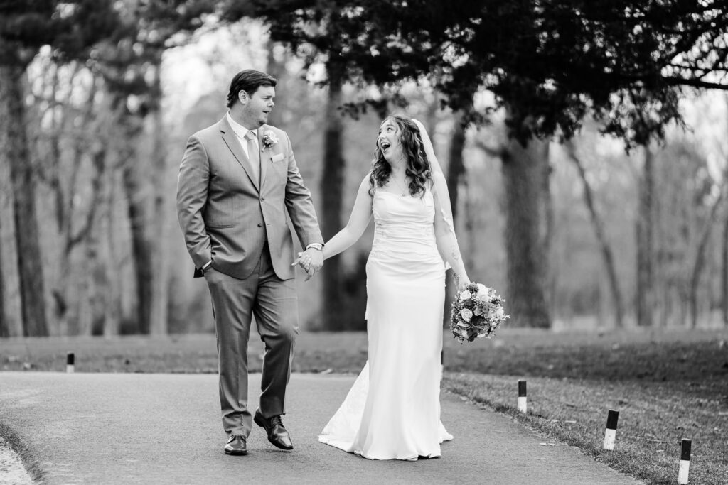 Black and white portrait of laughing bride and groom walking cart path at Pinelands Golf Club NJ