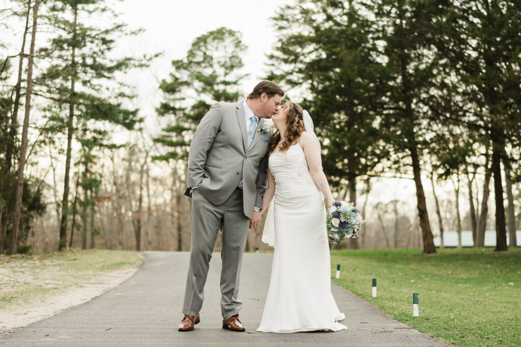 Bride and groom kissing on tree-lined cart path at Pinelands Golf Club outdoor wedding Hammonton NJ