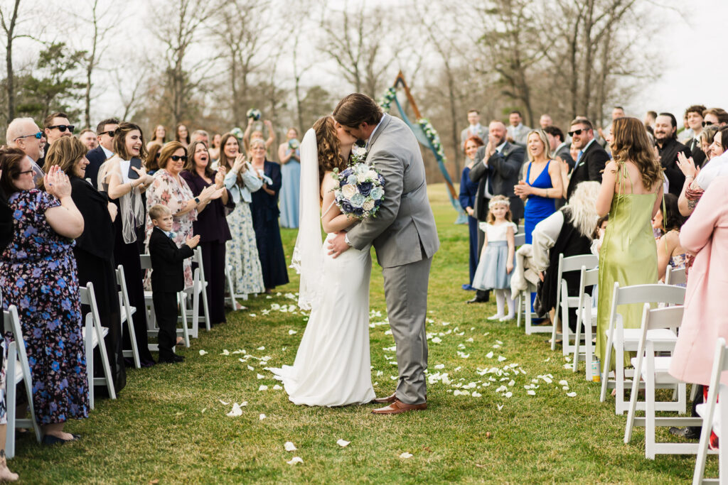 Bride and groom kissing mid-aisle during recessional at Pinelands Golf Club outdoor wedding New Jersey