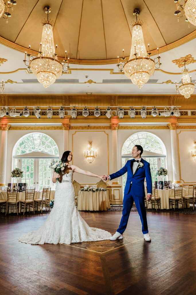 Bride and groom holding hands on the Crystal Plaza ballroom dance floor beneath the gold chandelier dome in Livingston NJ
