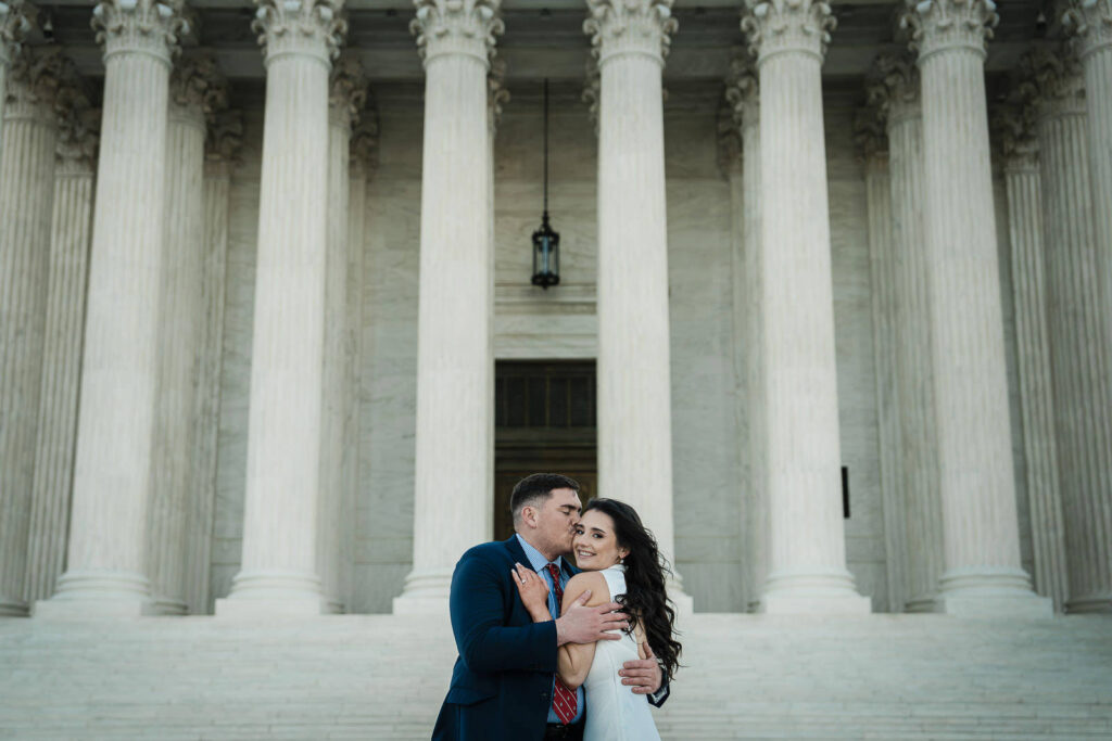 Man kissing his partner's cheek as she smiles in front of the Supreme Court columns Washington DC