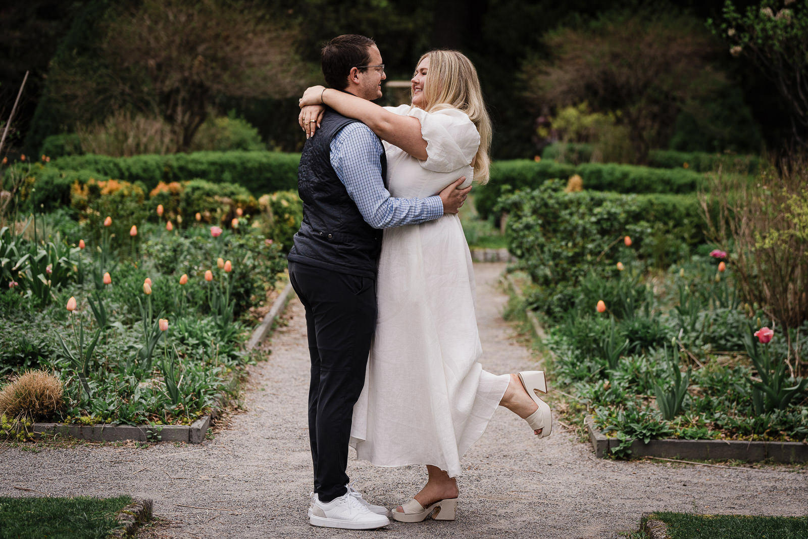 Newly engaged couple embracing joyfully on garden path at Van Vleck with tulips blooming