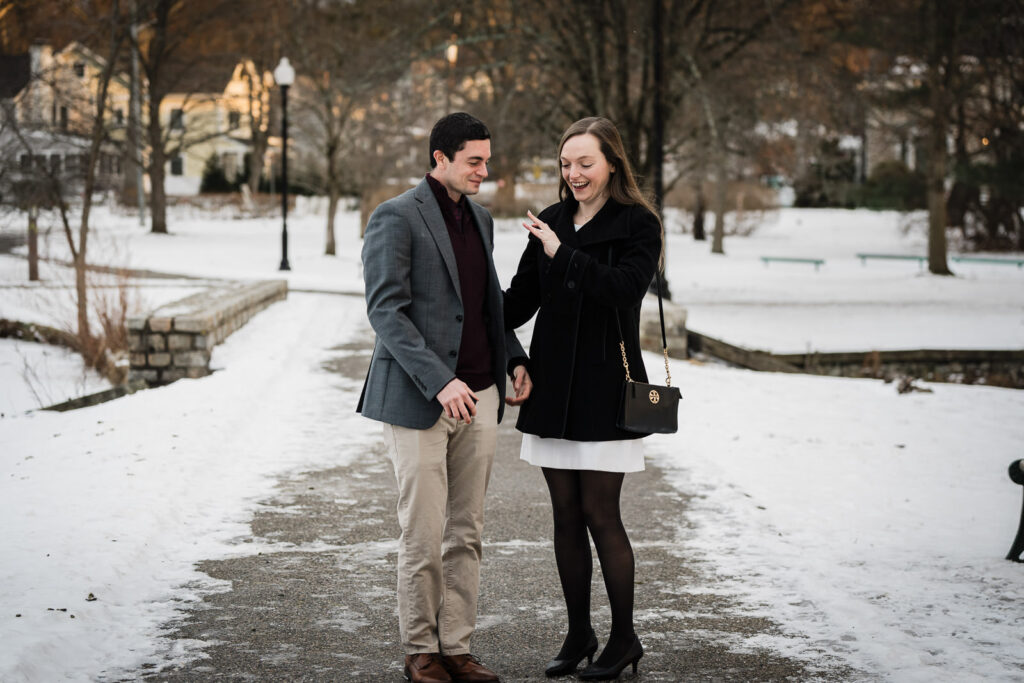 Newly engaged woman admiring ring and laughing with partner on snowy path in NJ