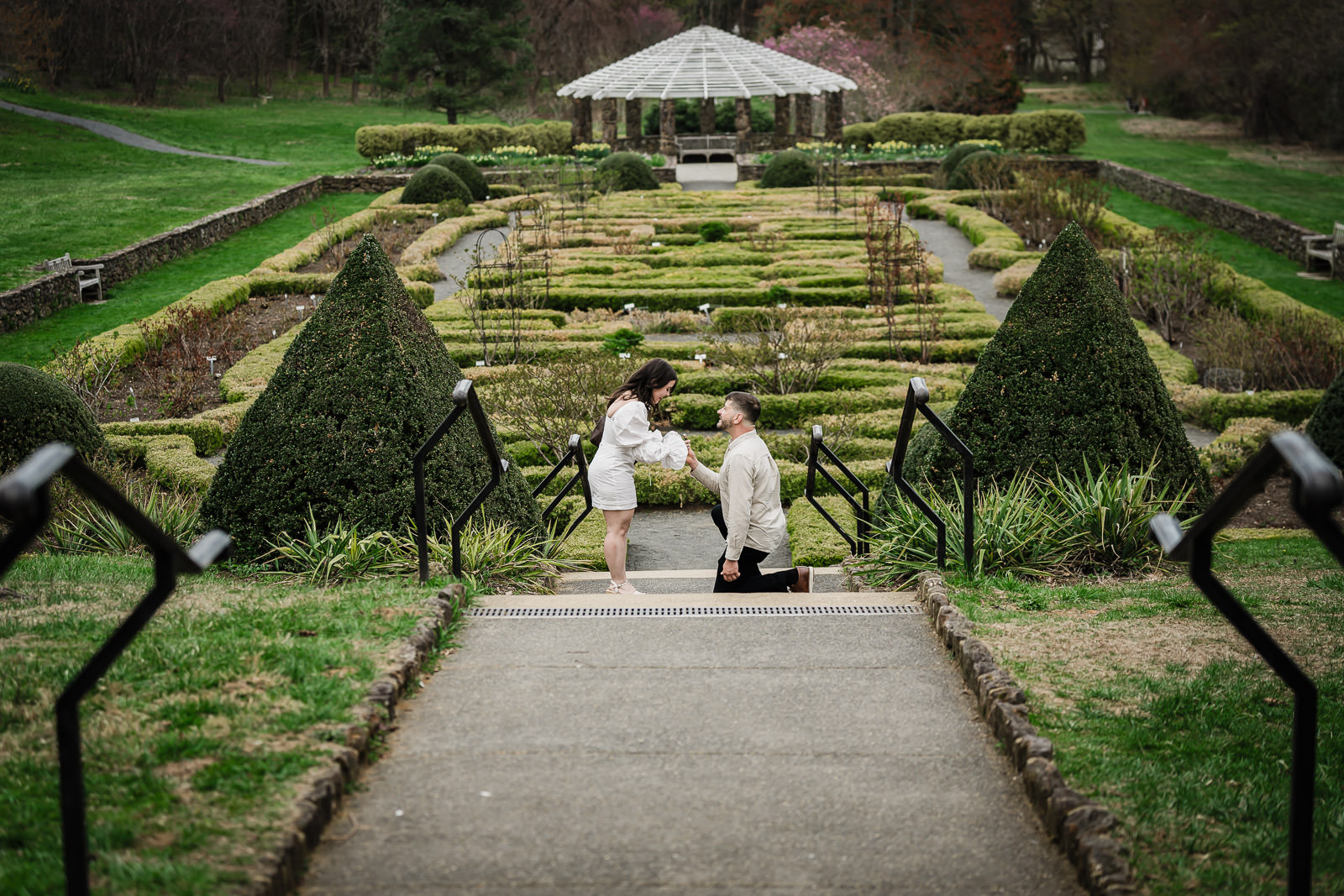 Luiz proposing to Dryellen at Deep Cut Gardens in Middletown NJ — the formal parterre garden and pavilion in the background