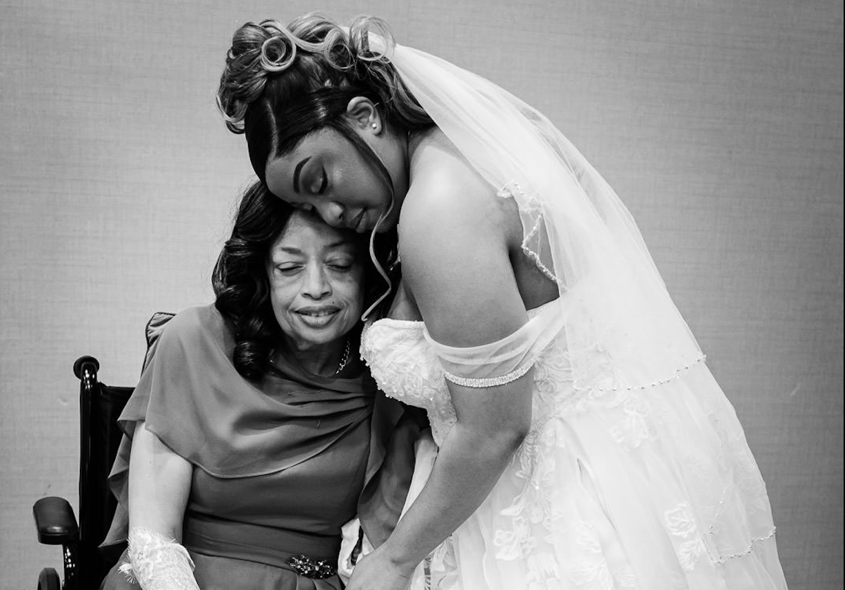 Black and white documentary wedding photo of a bride embracing her mother in a wheelchair during the getting ready moment