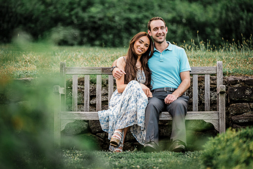 Newly engaged couple sitting relaxed and happy together on a garden bench at Deep Cut Gardens in Middletown New Jersey photographed by Alex Kaplan