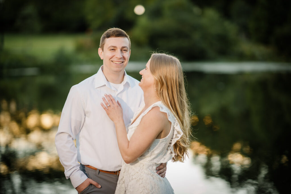 Couple laughing and holding each other close by a lake at golden hour in New Jersey after a romantic outdoor proposal photographed by Alex Kaplan