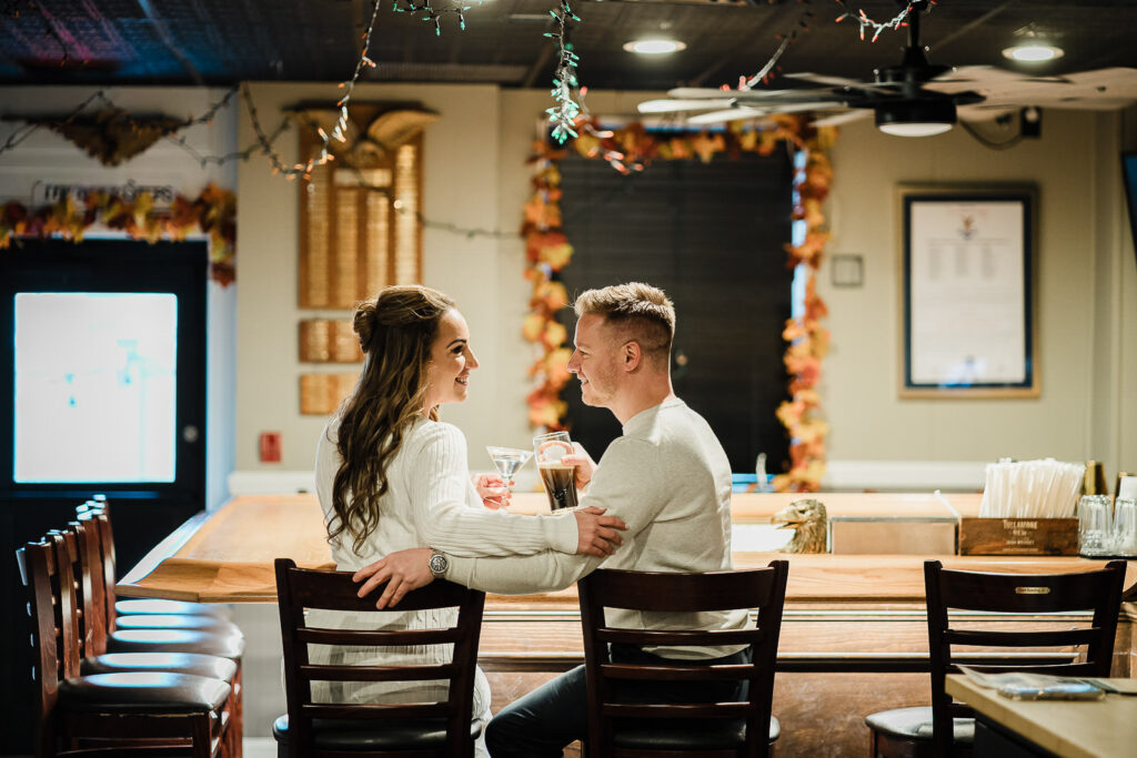 Couple sharing drinks and laughing together at warmly lit New Jersey bar engagement celebration