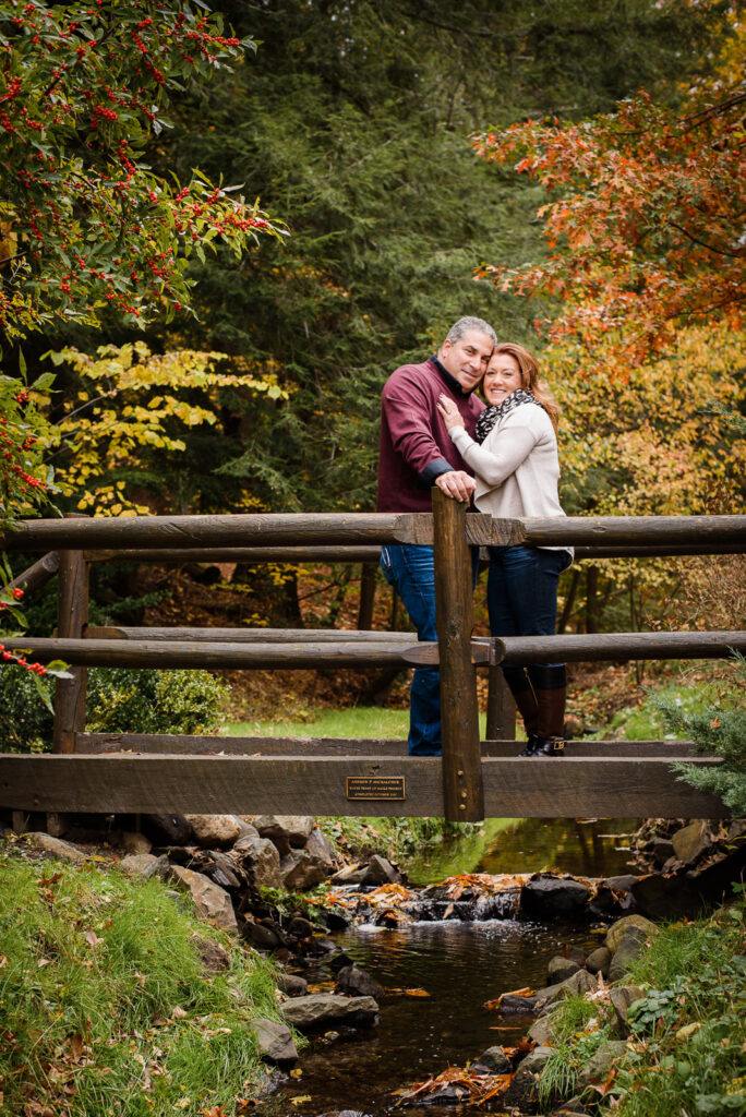 Couple on wooden bridge over creek during fall engagement session at Overpeck County Park Bergen County
