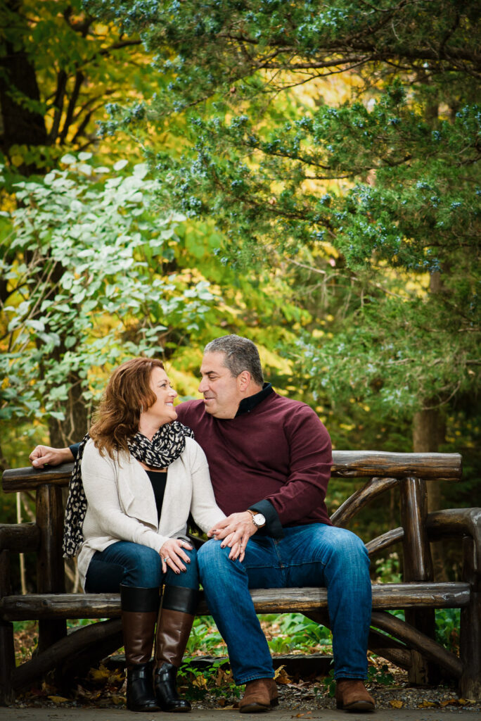 Couple on rustic log bench during fall engagement session at Overpeck County Park Bergen County NJ