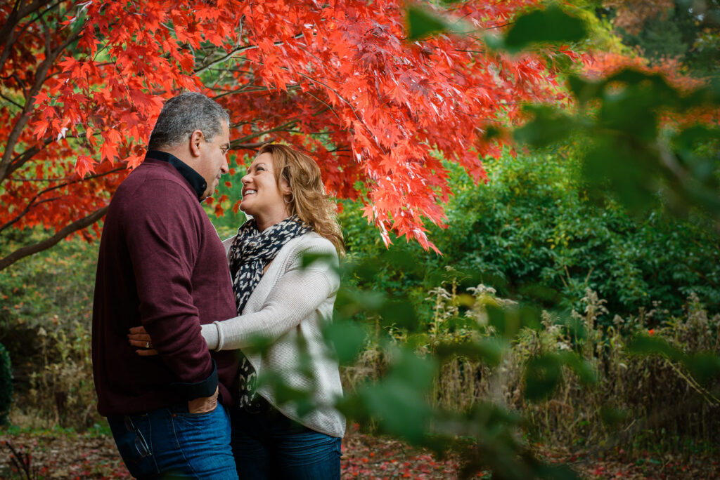 Couple laughing under red maple tree during fall engagement session at Overpeck County Park NJ