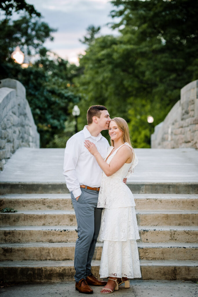 Couple standing together on the stone bridge at Verona Park New Jersey during a romantic outdoor proposal session at sunset photographed by Alex Kaplan
