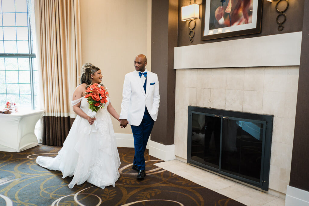 Bride and groom walking together past stone fireplace in Sheraton Parsippany Hotel wedding lobby