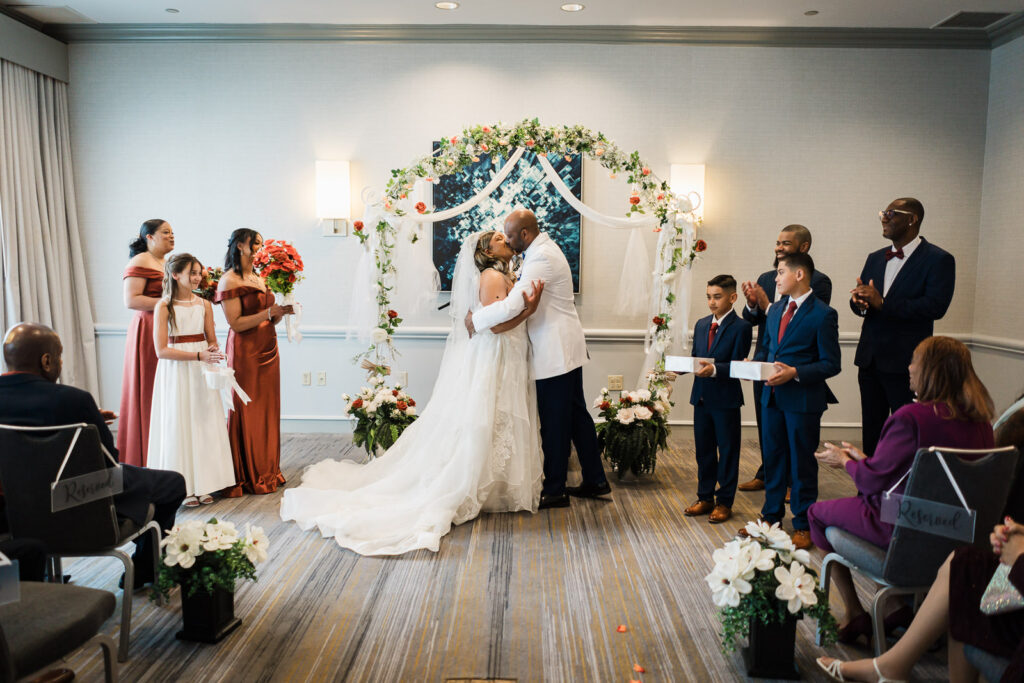 Bride and groom sharing first kiss beneath floral arch at Sheraton Parsippany Hotel NJ ceremony