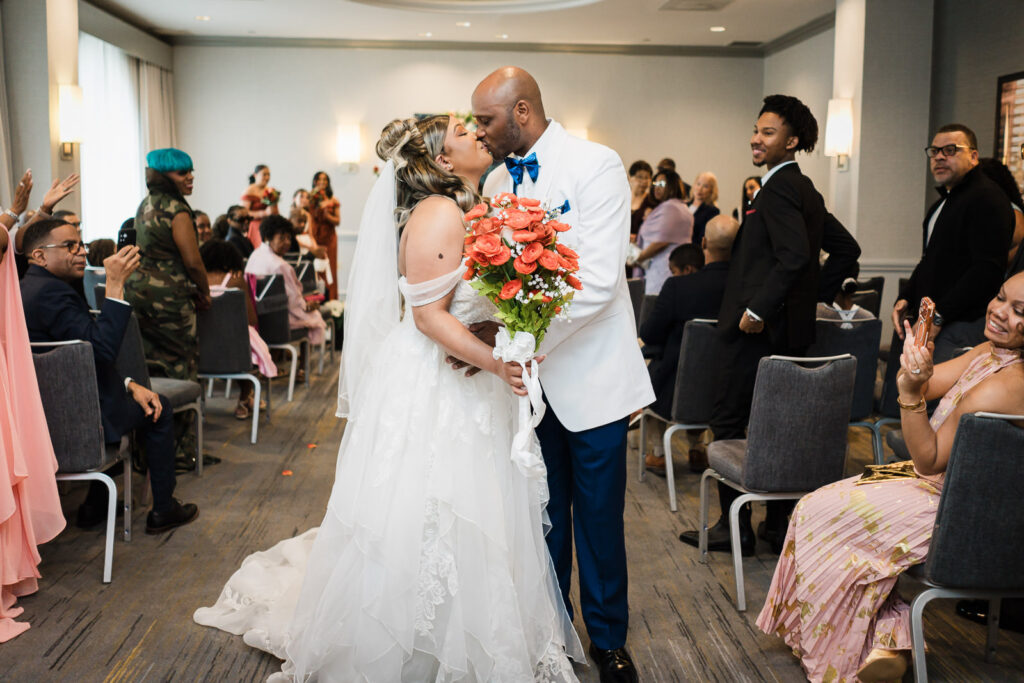 Couple kissing mid-recessional as guests stand and cheer at Sheraton Parsippany Hotel New Jersey wedding