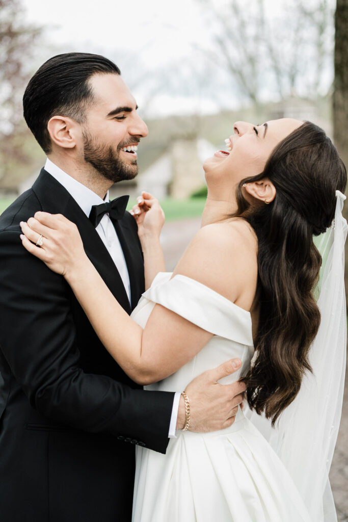 Bride Kiara laughing with her head thrown back in Otari's arms during
outdoor wedding portraits at Waterloo Village New Jersey