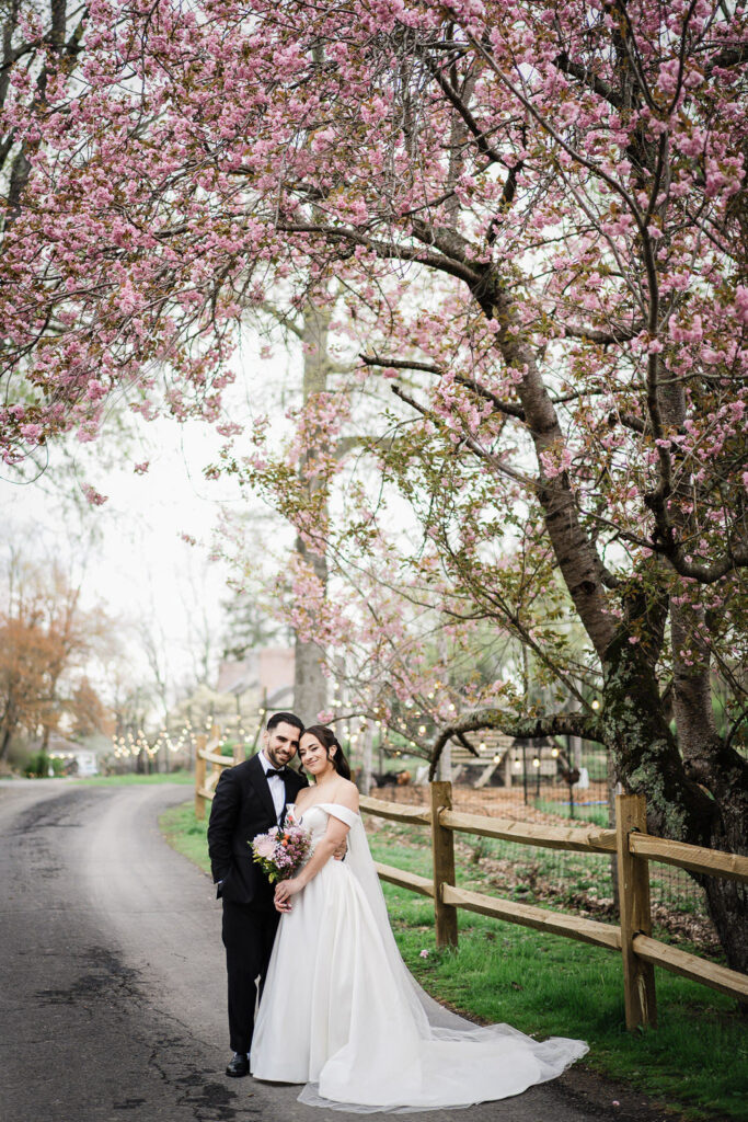 Bride and groom leaning together under blooming cherry blossom trees during spring wedding portraits at Waterloo Village New Jersey