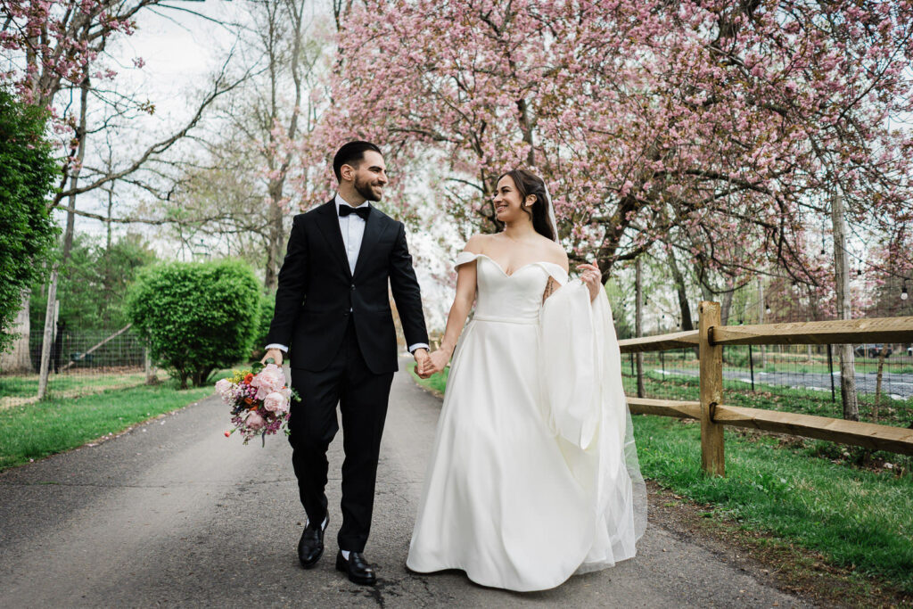 Bride and groom walking hand in hand along the cherry blossom lined path at Waterloo Village wedding in New Jersey