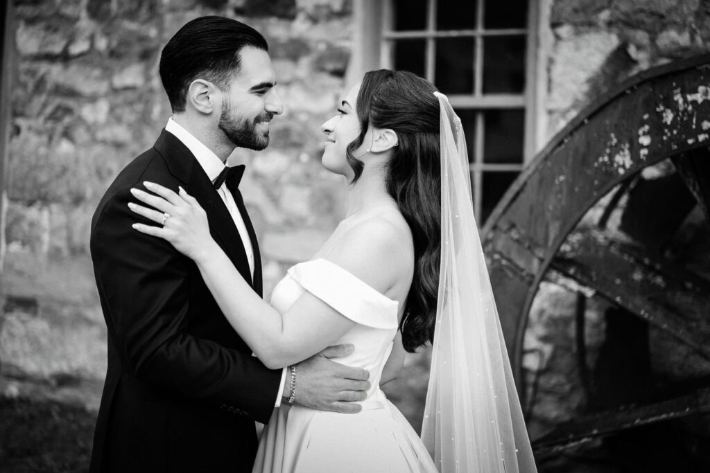 Black and white portrait of Kiara and Otari embracing in front of the
historic stone wall and water wheel at Waterloo Village wedding in
New Jersey