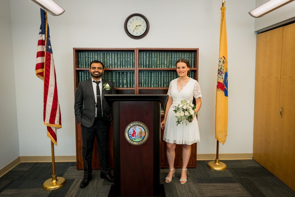 Couple posing inside the Bergen County Clerk's Office ceremony room with the Bergen County seal and flags in Hackensack New Jersey