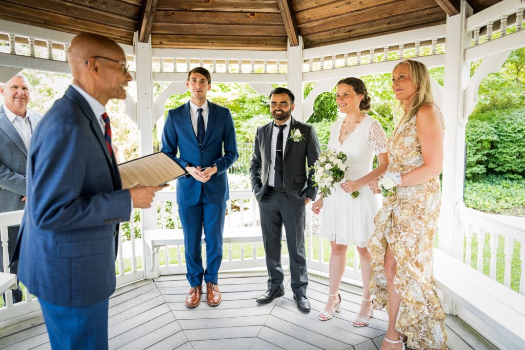 Couple standing with officiant and witnesses during intimate wedding ceremony at Bergen County Plaza gazebo in Hackensack New Jersey