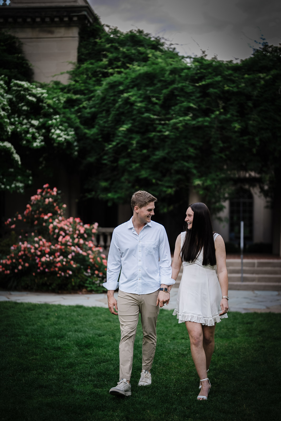 Newly engaged couple walking past blooming roses on the grounds of Van Vleck House & Gardens