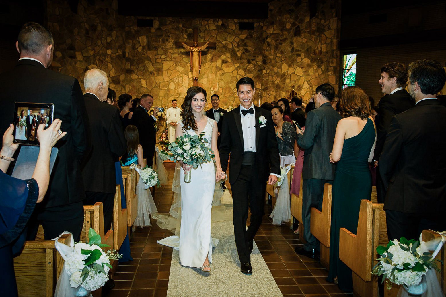 Newlywed couple smiling and holding hands during their recessional at a Catholic church wedding ceremony