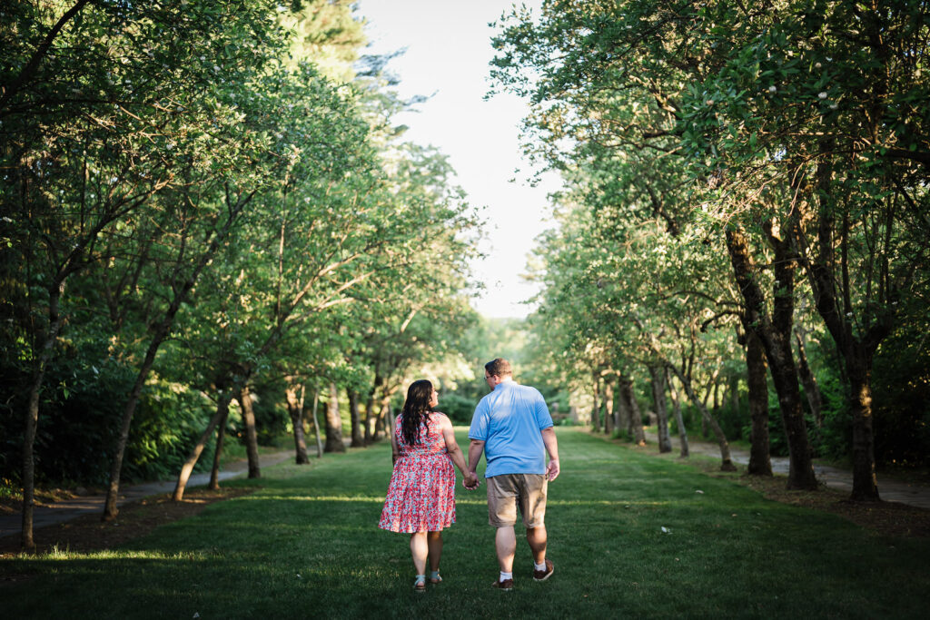 Engaged couple walking a tree-lined garden allée at Skylands Manor in Ringwood New Jersey