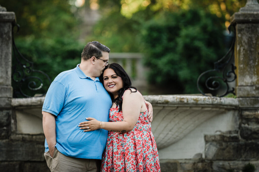 Engaged couple leaning on a stone wall beside the water at Skylands Manor Ringwood