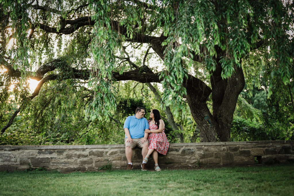 Engaged couple sitting beneath a willow tree at golden hour at Skylands Manor Ringwood
