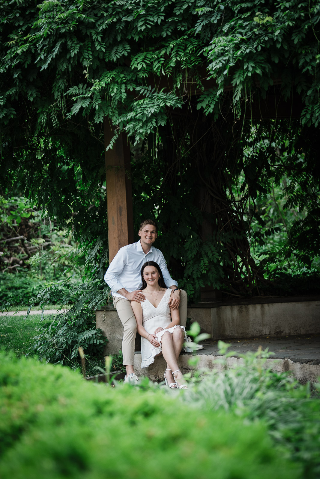 Engagement portrait of a smiling couple beneath the wisteria pergola at Van Vleck Gardens Montclair NJ
