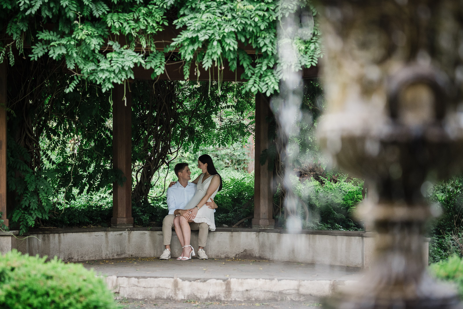 Engaged couple seated under the Van Vleck pergola with a garden fountain in the foreground