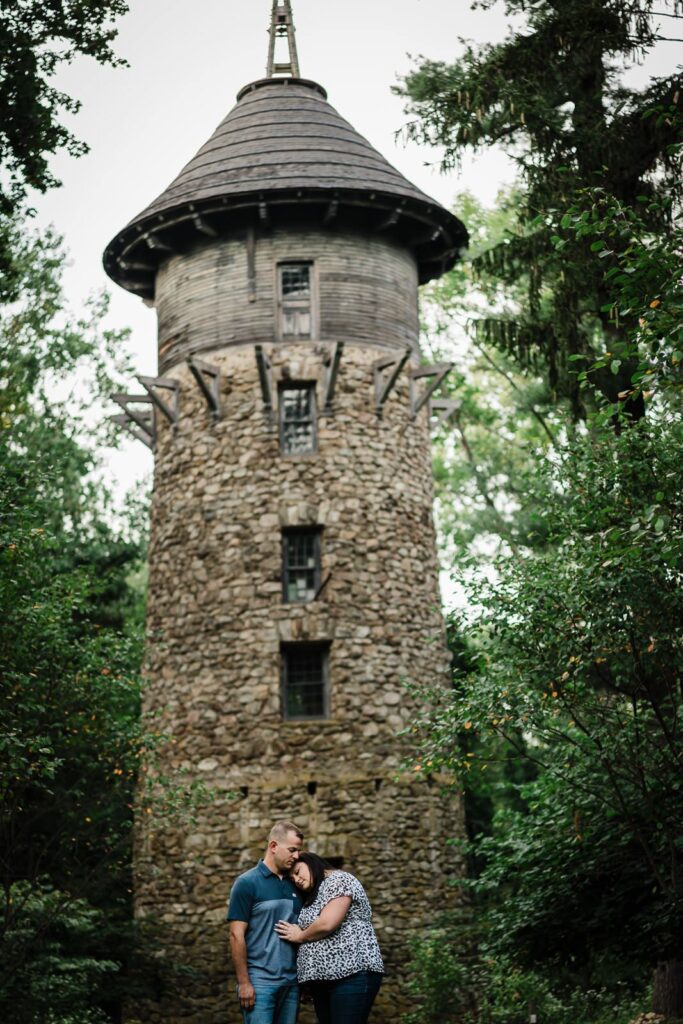 Engaged couple embracing beneath the historic stone tower at Crossed Keys Estate in Andover NJ