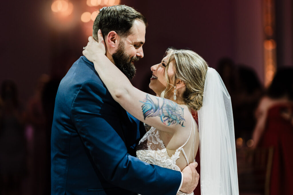 Bride and groom dancing closely under warm chandelier light at their wedding reception.