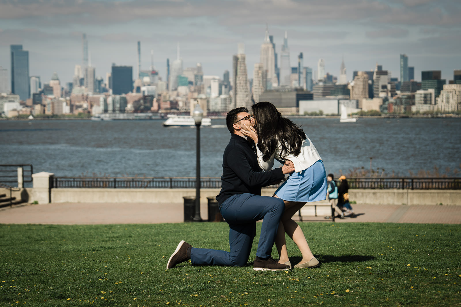 Man kneeling to propose to his partner on a New Jersey waterfront facing the Manhattan skyline.