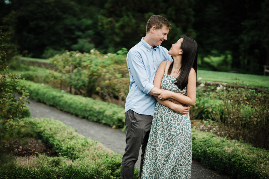 Andrew and Emily embracing on a boxwood lined path at Deep Cut Gardens NJ