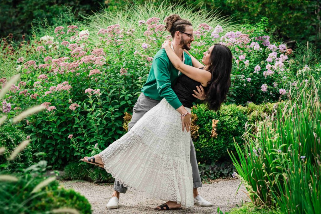 Engaged couple dancing on a gravel path beside blooming perennial beds at Deep Cut Gardens