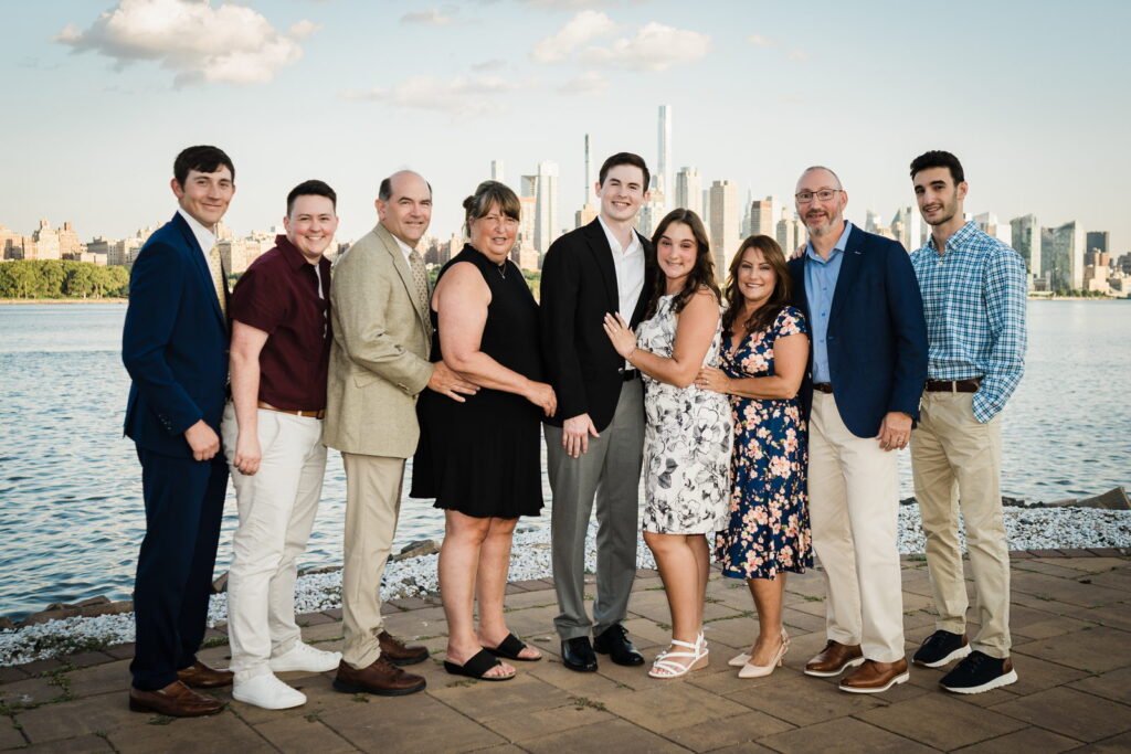 Newly engaged couple with family in group portrait on waterfront walkway after proposal