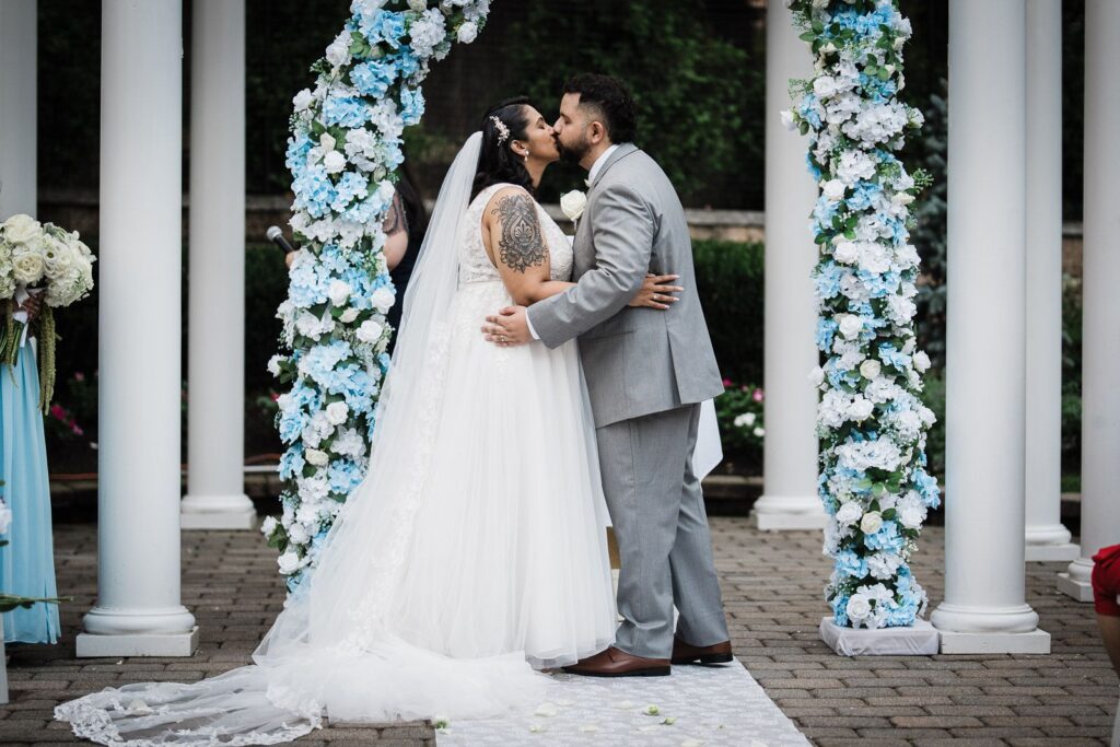Couple kissing beneath a floral ceremony arch at a New Jersey wedding venue