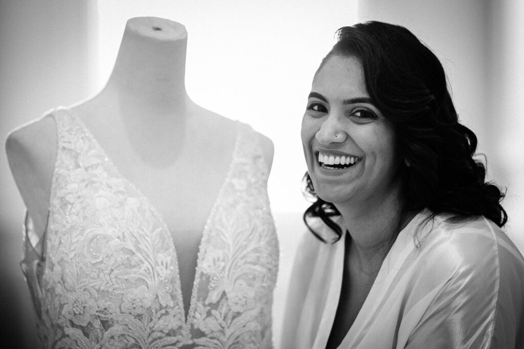 Bride laughing beside her gown while getting ready before a New Jersey wedding ceremony