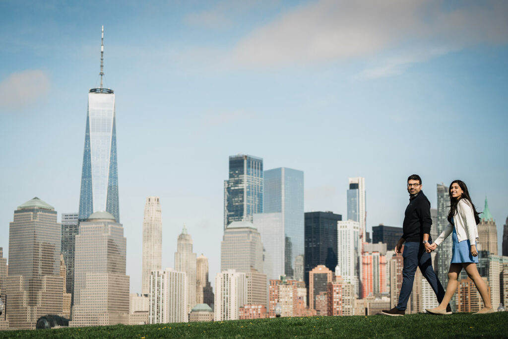 Newly engaged couple walking hand in hand with Lower Manhattan in the background