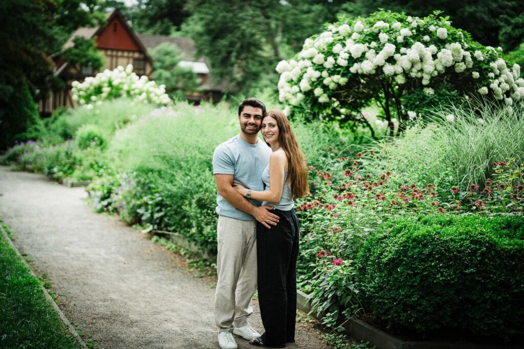 Engaged couple standing on a gravel garden path among hydrangeas at Van Vleck Montclair