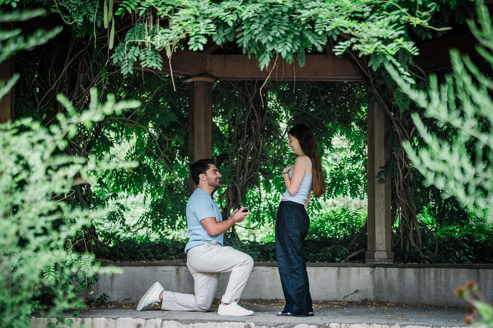 Man kneeling to propose beneath a vine-covered pergola at Van Vleck House and Gardens