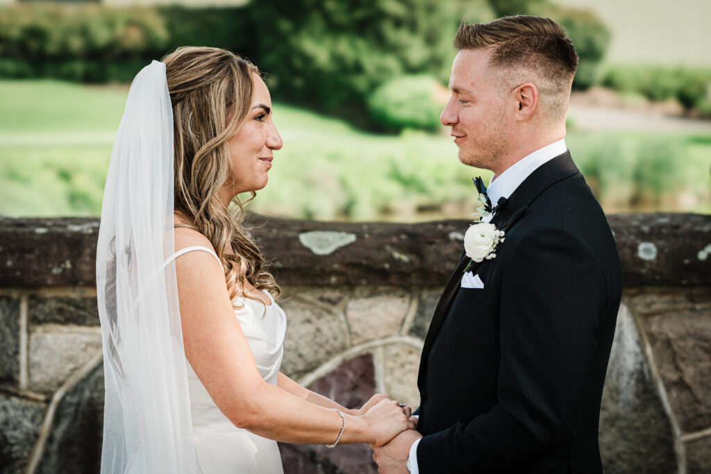 Ilysse and James holding hands beside the stone wall at Brooklake Country Club